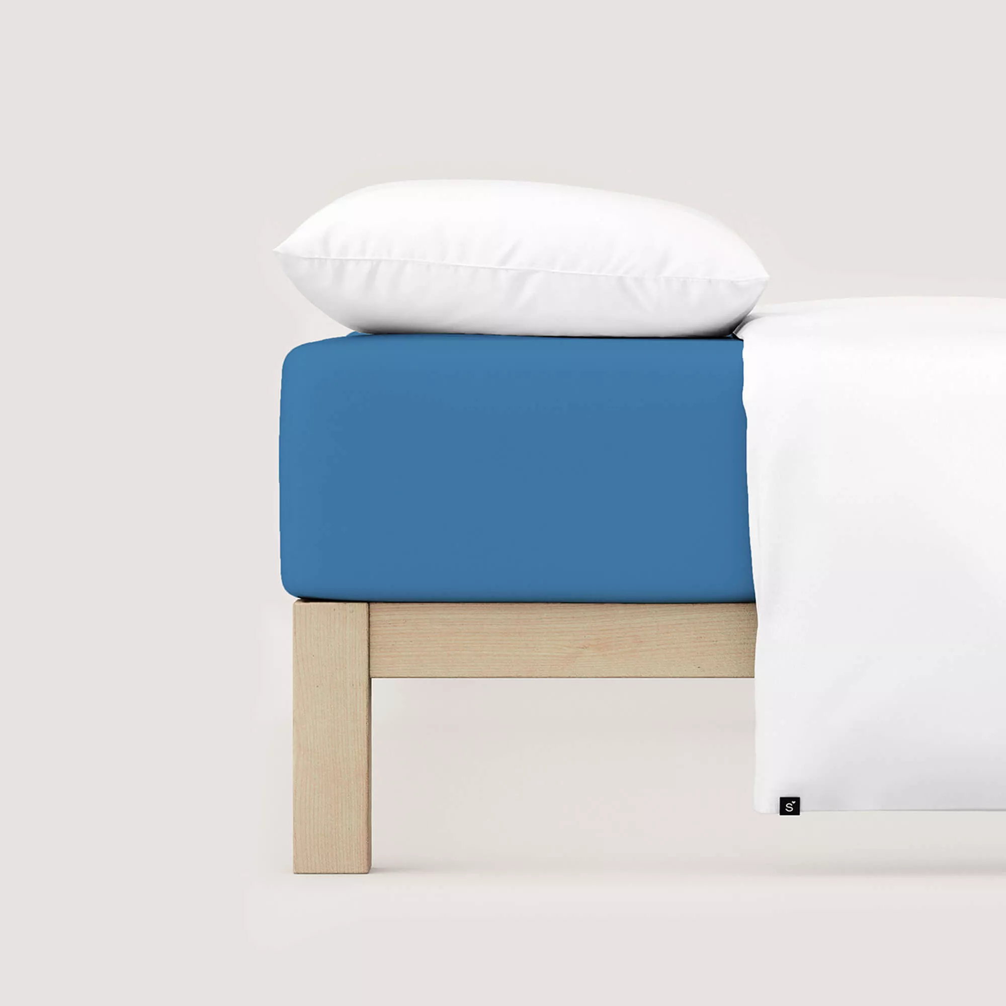 Spannbettlaken Pure von Schlafgut in Farbe blue mid aus 95% Bio-Baumwolle und 5% Elasthan auf Bett mit Kissen und Decke